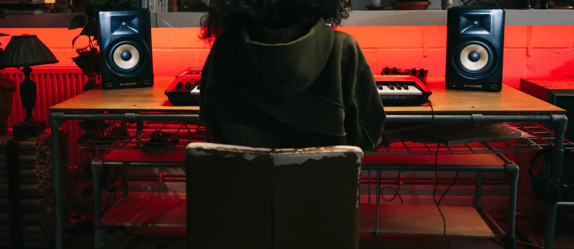 Home-studio avec deux enceintes Forty Sixty de part et d'autre d'un bureau, un clavier et un musicien de dos