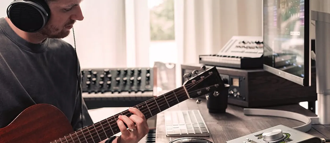 Musicien au casque jouant de la guitare acoustique près d'un Apollo Twin X Gen 2 posé sur le bureau