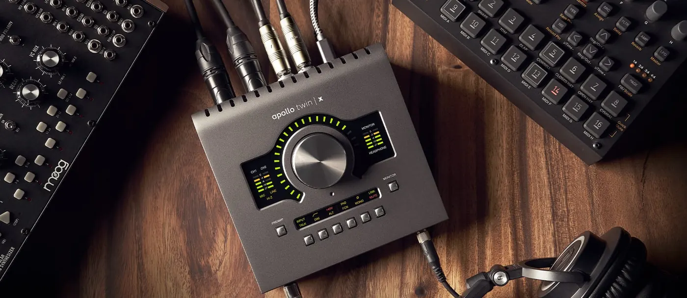 Apollo Twin X USB vu de dessus sur un bureau en bois, câbles branchés à l'arrière, entre un clavier de synthétiseur et un casque
