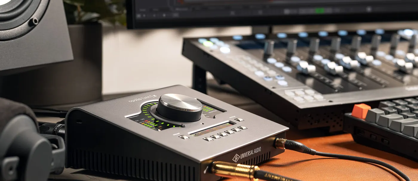 Apollo Twin X USB sur un bureau de studio, câble jack branché en façade, surface de contrôle et moniteur en arrière-plan