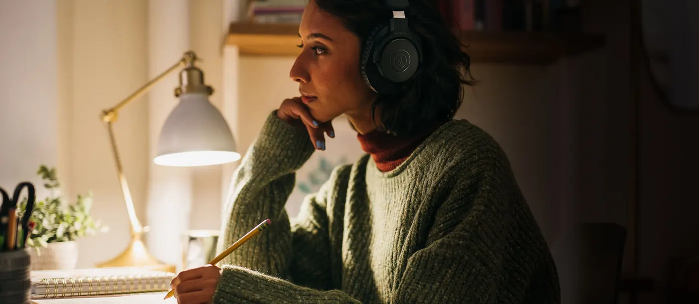 Jeune femme à son bureau le soir, casque ATH-M20xBT sur les oreilles