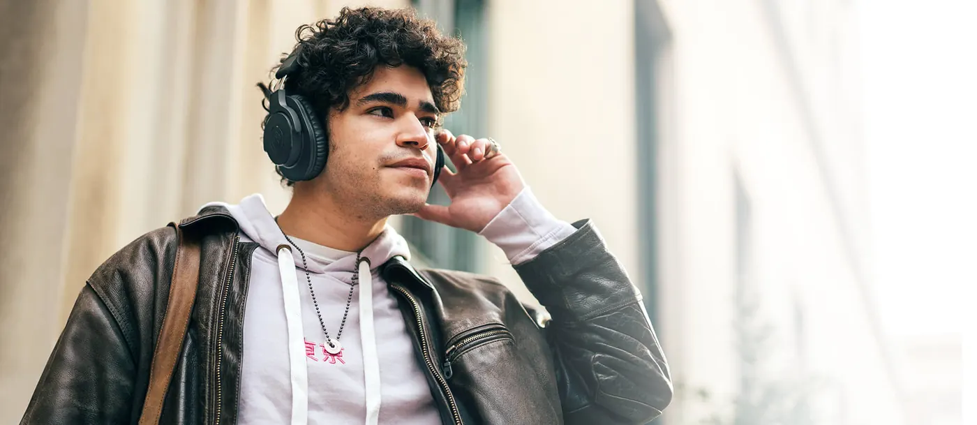 Jeune homme en ville portant le casque ATH-M20xBT noir, une main sur l'oreillette