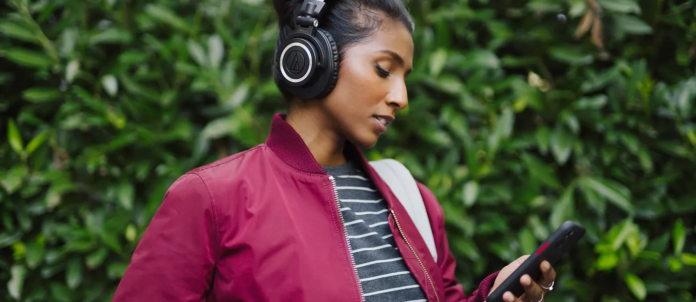 Femme en veste rose consultant son téléphone, casque ATH-M50xBT2 noir sur les oreilles