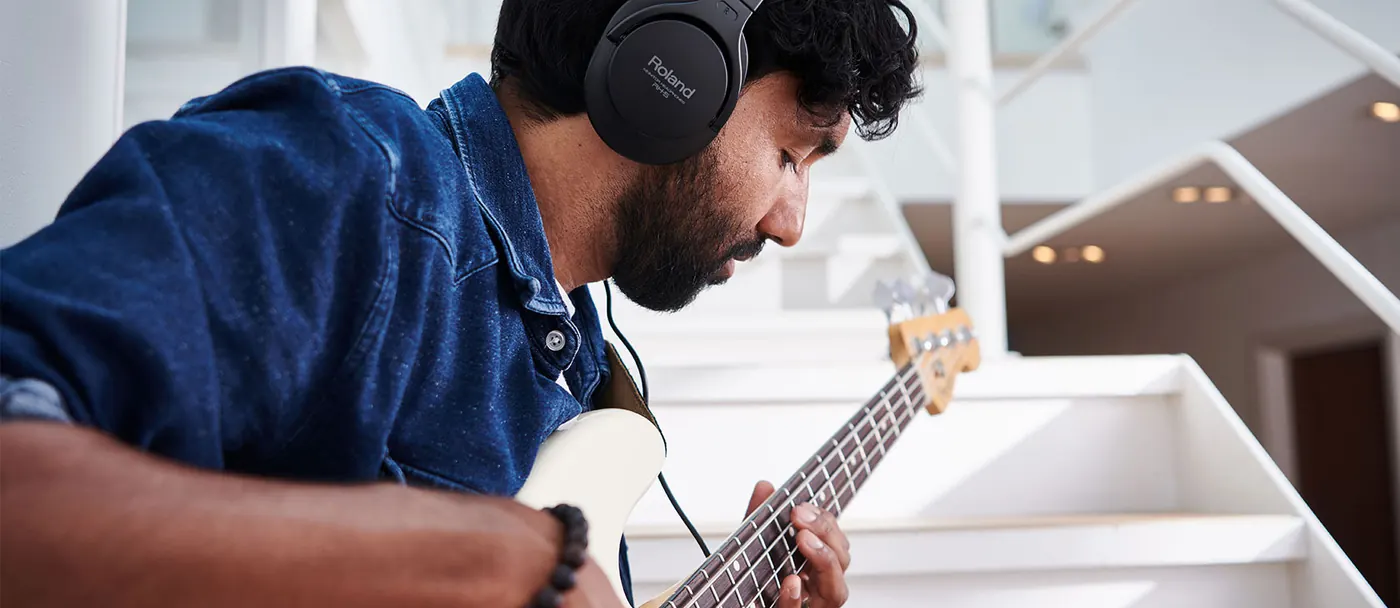 Bassiste jouant avec le casque Roland RH-5 sur les oreilles, assis dans un escalier