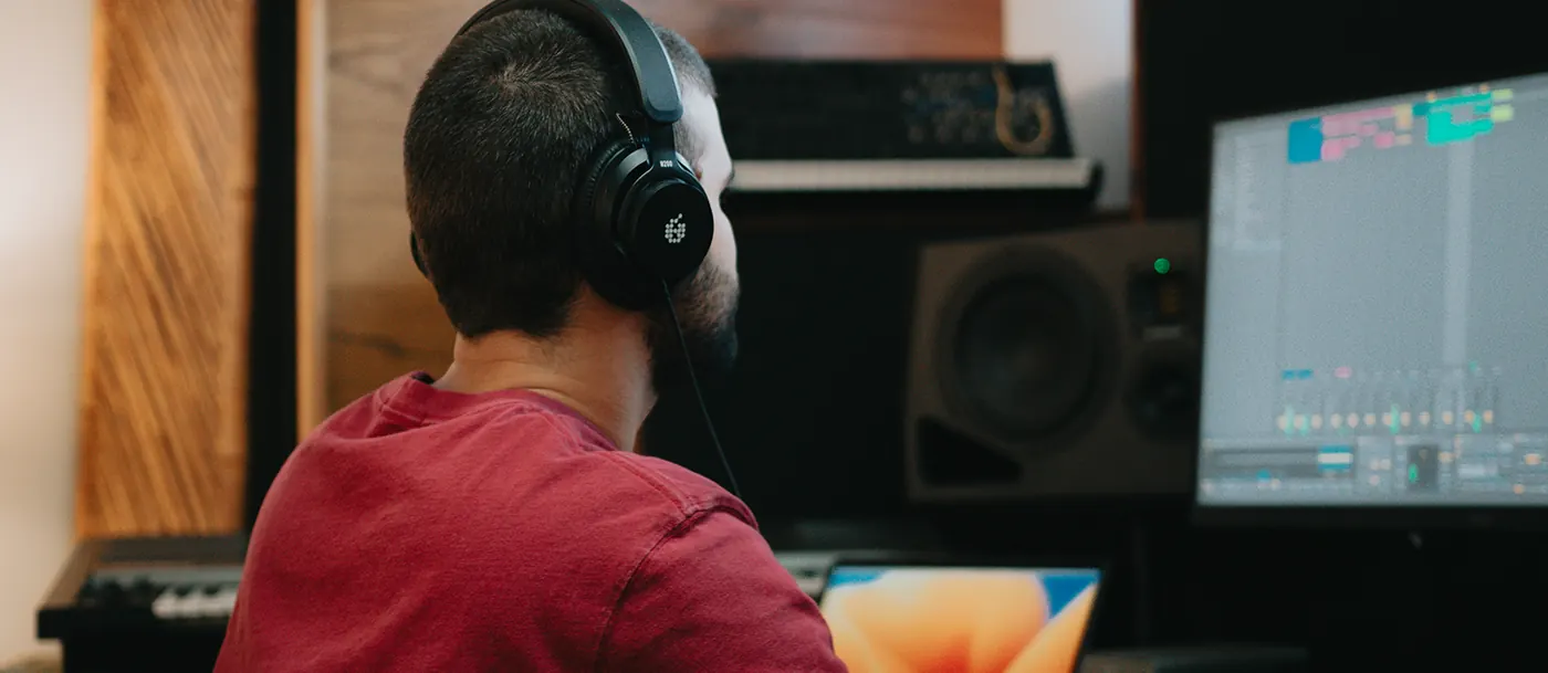 Musicien de dos portant le casque ADAM Audio H200 devant un écran de station audionumérique, moniteurs en arrière-plan