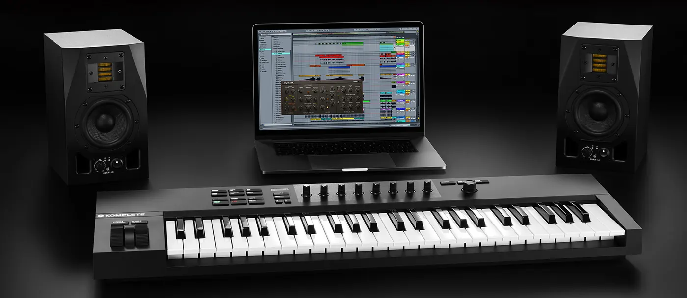 Komplete Kontrol A49 posé devant un ordinateur portable et deux enceintes de monitoring sur un bureau sombre
