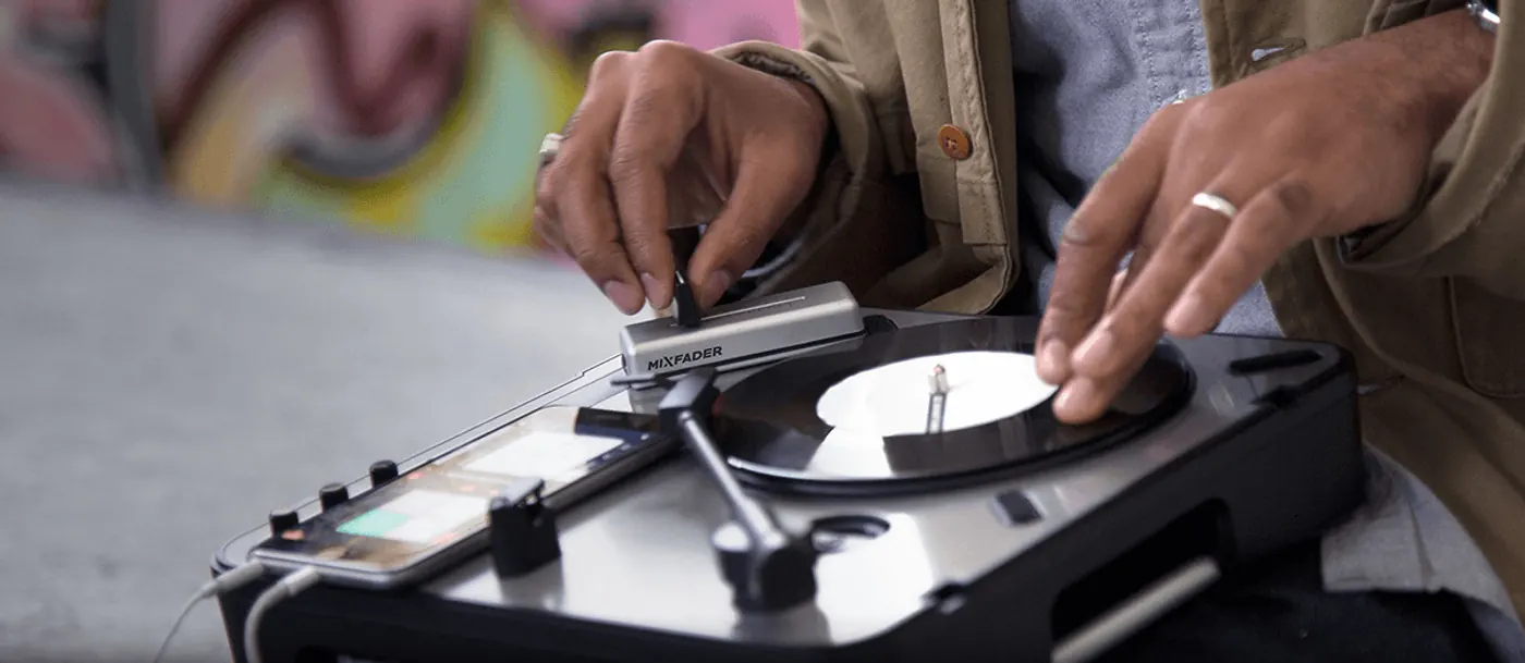 DJ scratchant sur une platine portable, le Mixfader posé à côté du disque, un smartphone relié à la platine