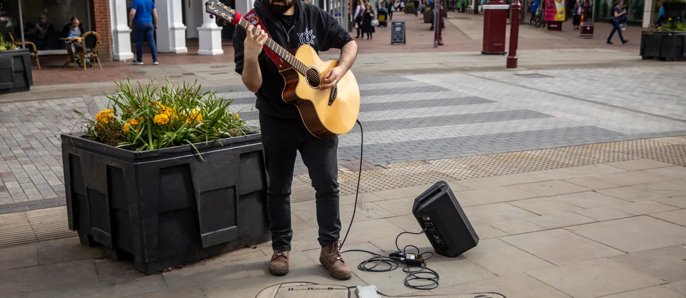 Guitariste jouant dans une rue piétonne avec une enceinte EVERSE 8 noire posée au sol