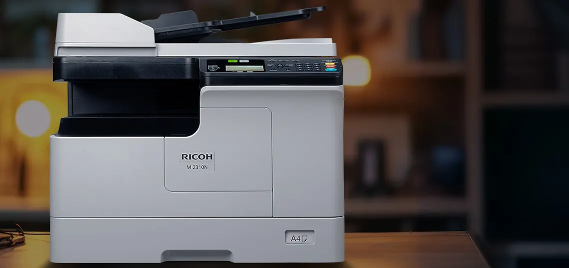 Ricoh M 2310N posée sur un plan de travail en bois dans un bureau, chargeur ARDF relevé