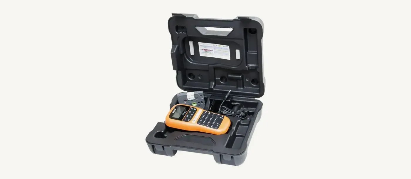 Mallette rigide Brother P-touch ouverte&nbsp;: calage moul&eacute; avec l&rsquo;&eacute;tiqueteuse PT-E110VP, une cassette de ruban et l&rsquo;adaptateur secteur